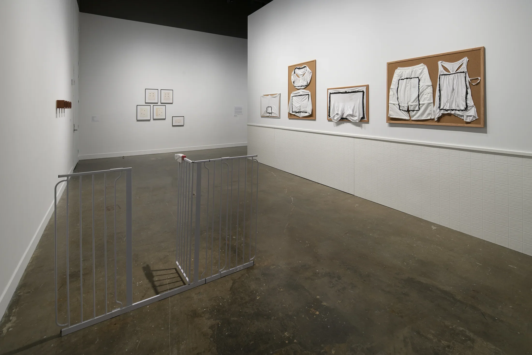 A freestanding gate with an open door, 4 bulletin boards with painted underwear to the right, 5 framed objects to the rear.