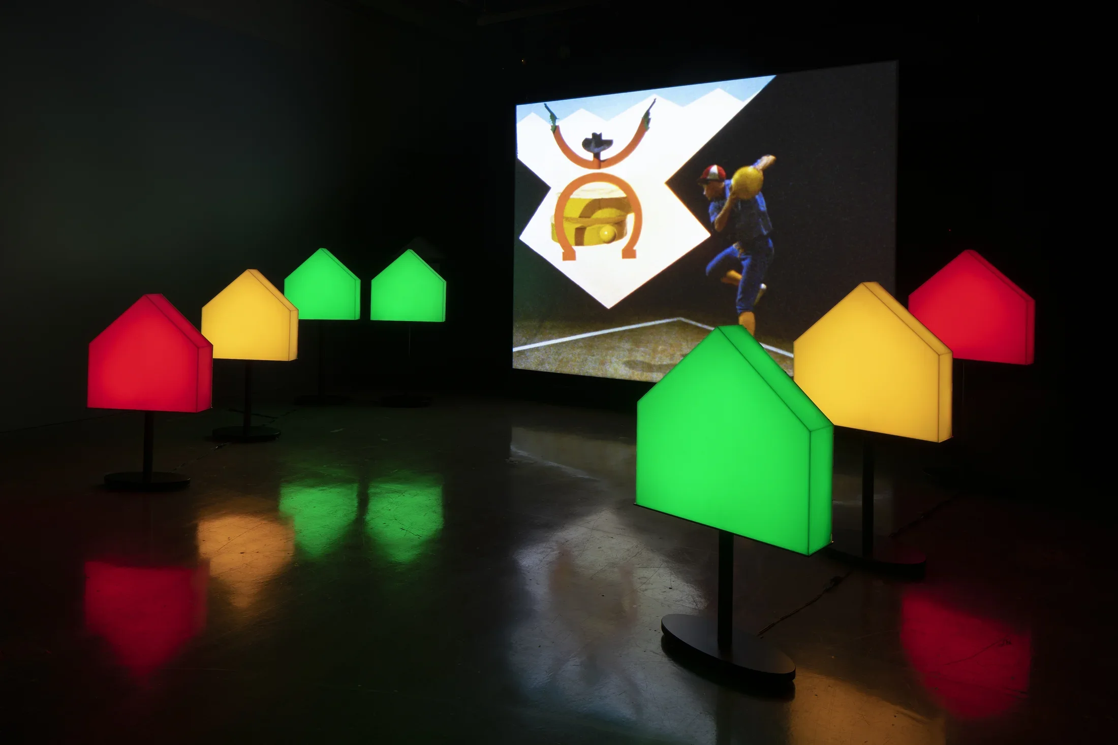 Colored pentagons flank a screen on which an image of a man in a blue jumpsuit and a stick drawing of a cowboy are projected.