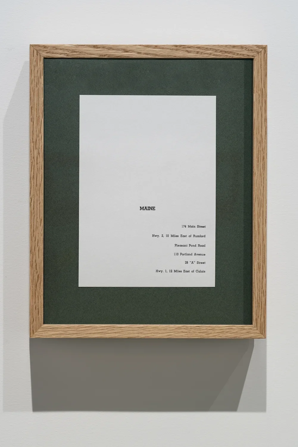 A vertical wooden frame with green matting and a piece of paper on which the name, Maine and 6 partial addresses are typed.