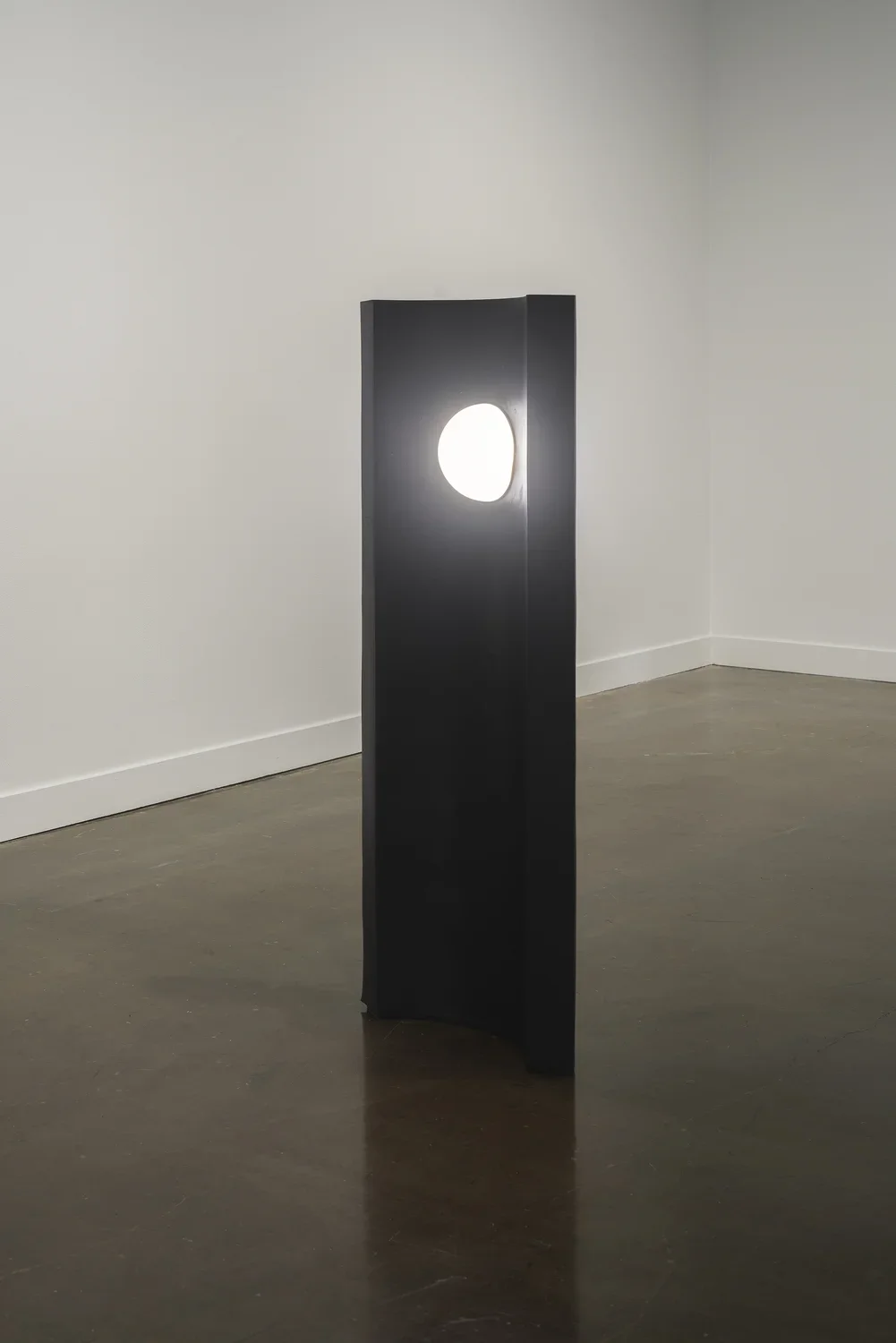 A convex, black tower with an orb of light in the center near the top stands alone in the Gallery.