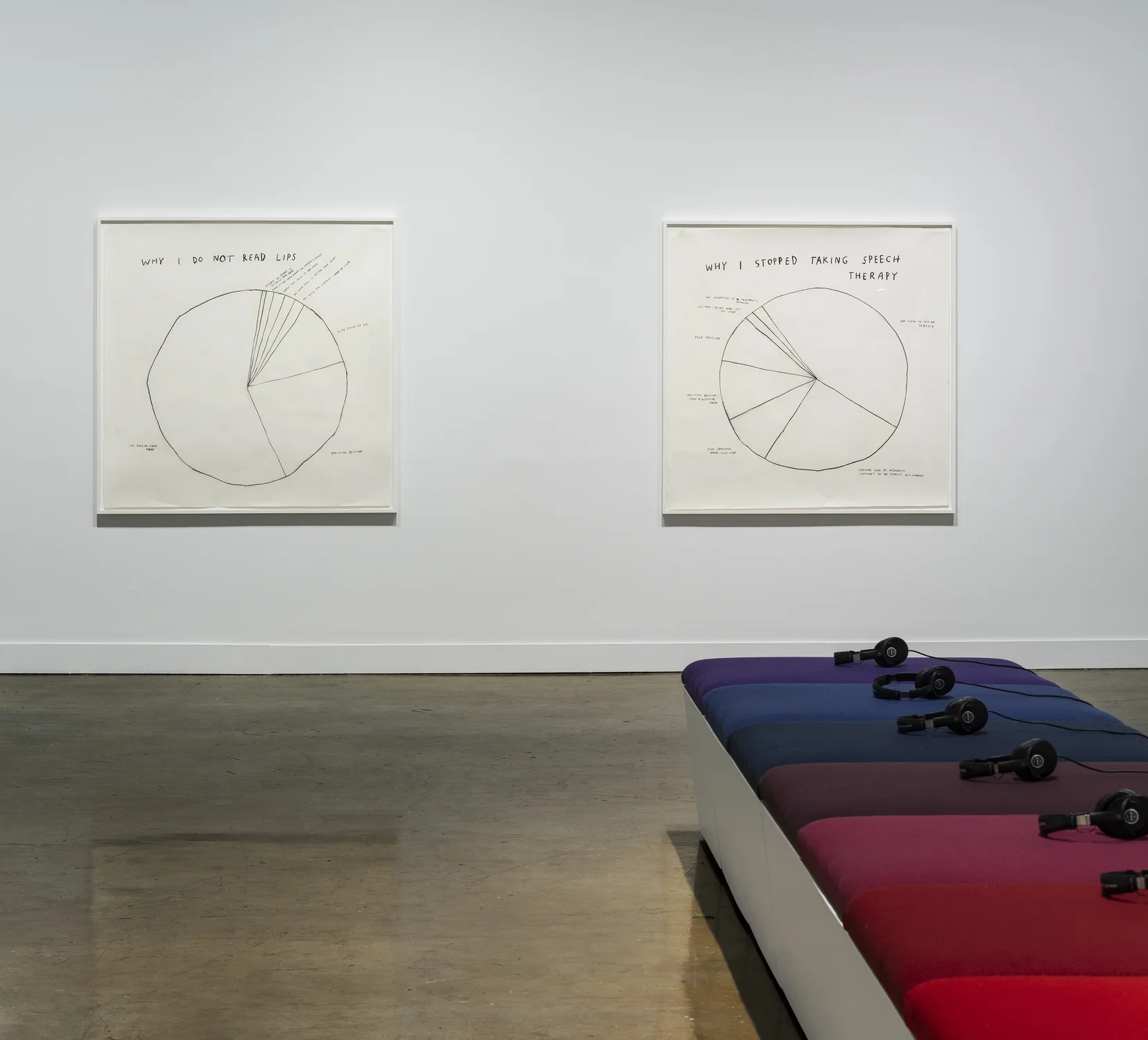 Bench with red, blue and purple cushions and headphones point to 2 framed, black and white pie-chart drawings on the wall.