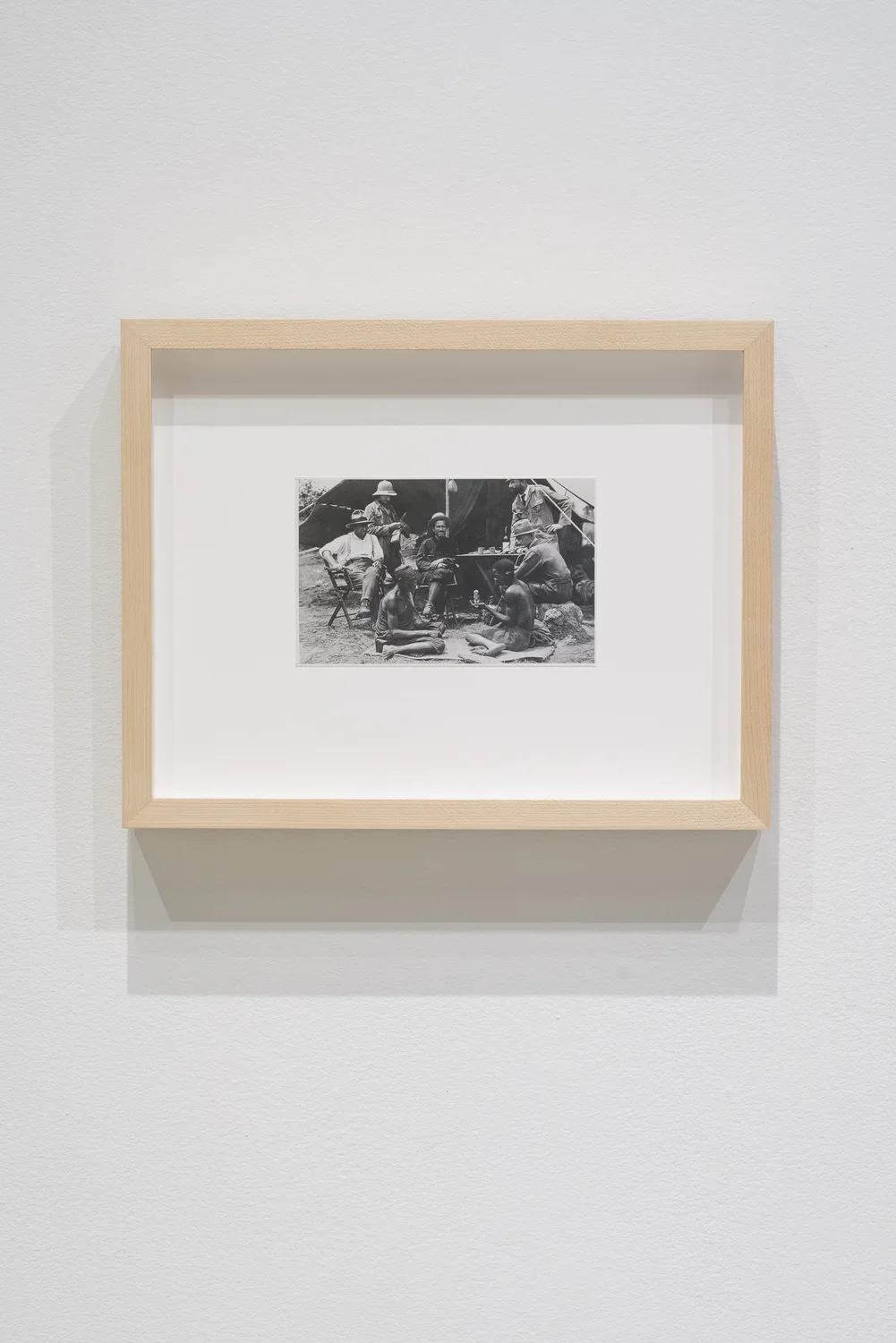 Framed black and white photograph of archaeologists seated around Angolan people. 