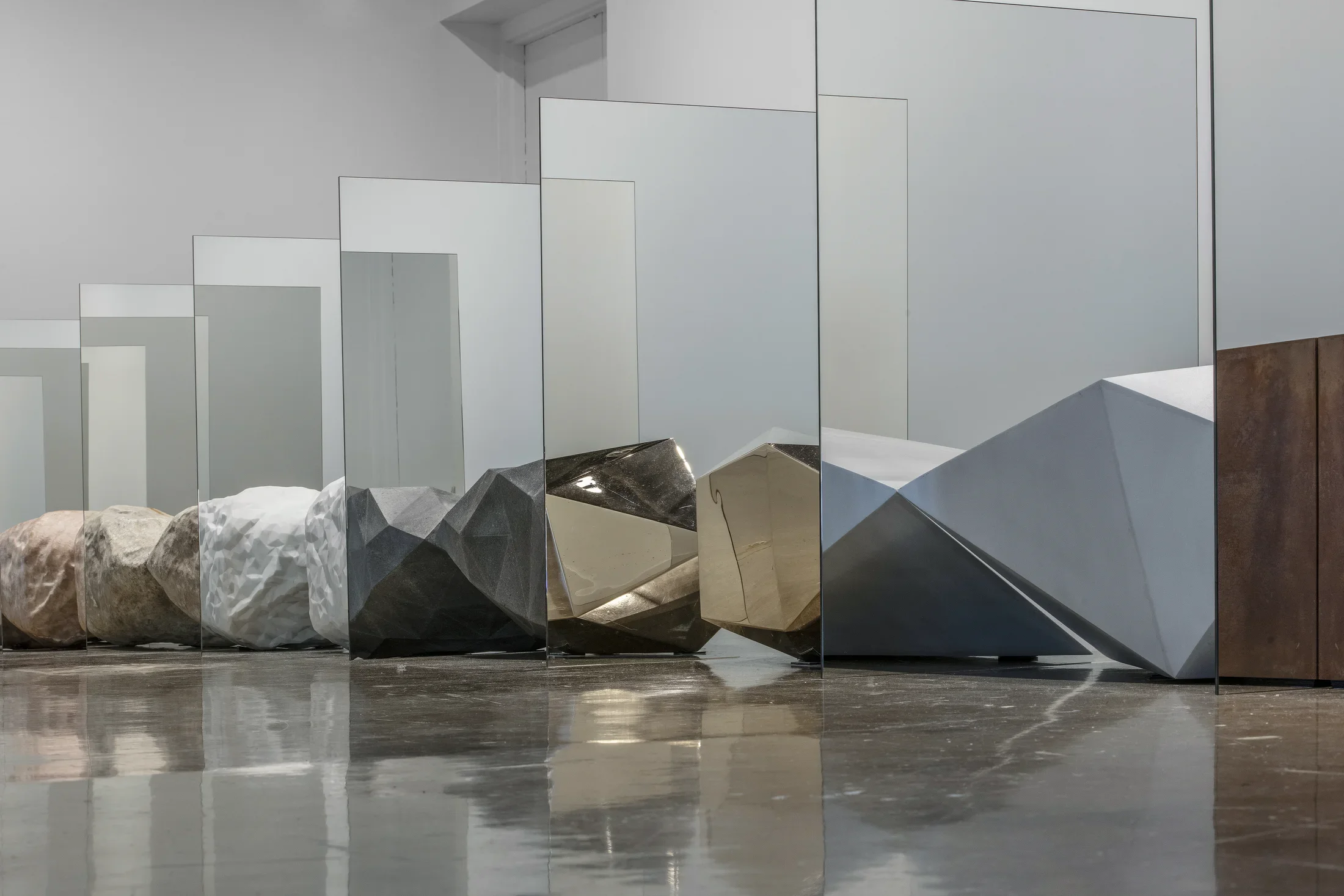 Detail view of objects resembling precious rocks are arraged in a straight row. Between each object is a mirror, creating the illusion that each rock is morphing into one another.