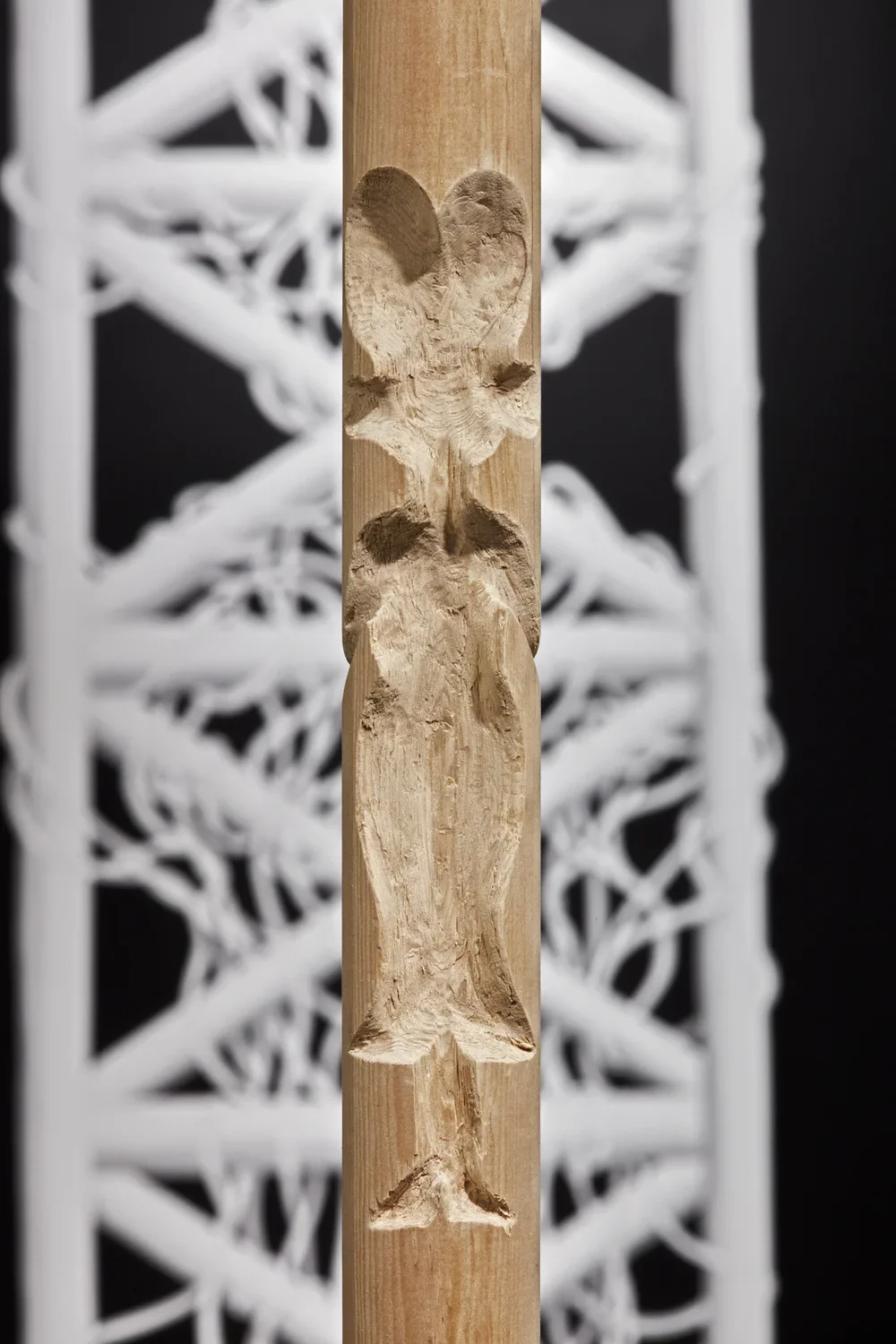 Detail view of woodel pole at center of gallery with the small cutout shape of a female figure with large hair.
