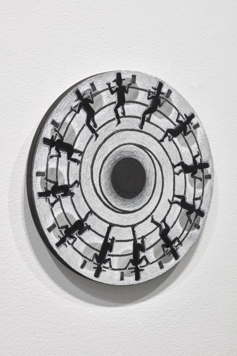 Detail side angle view of small wooden circle affixed to gallery wall with charcoal illustrations of a man wearing a tall hat climbing a rope.