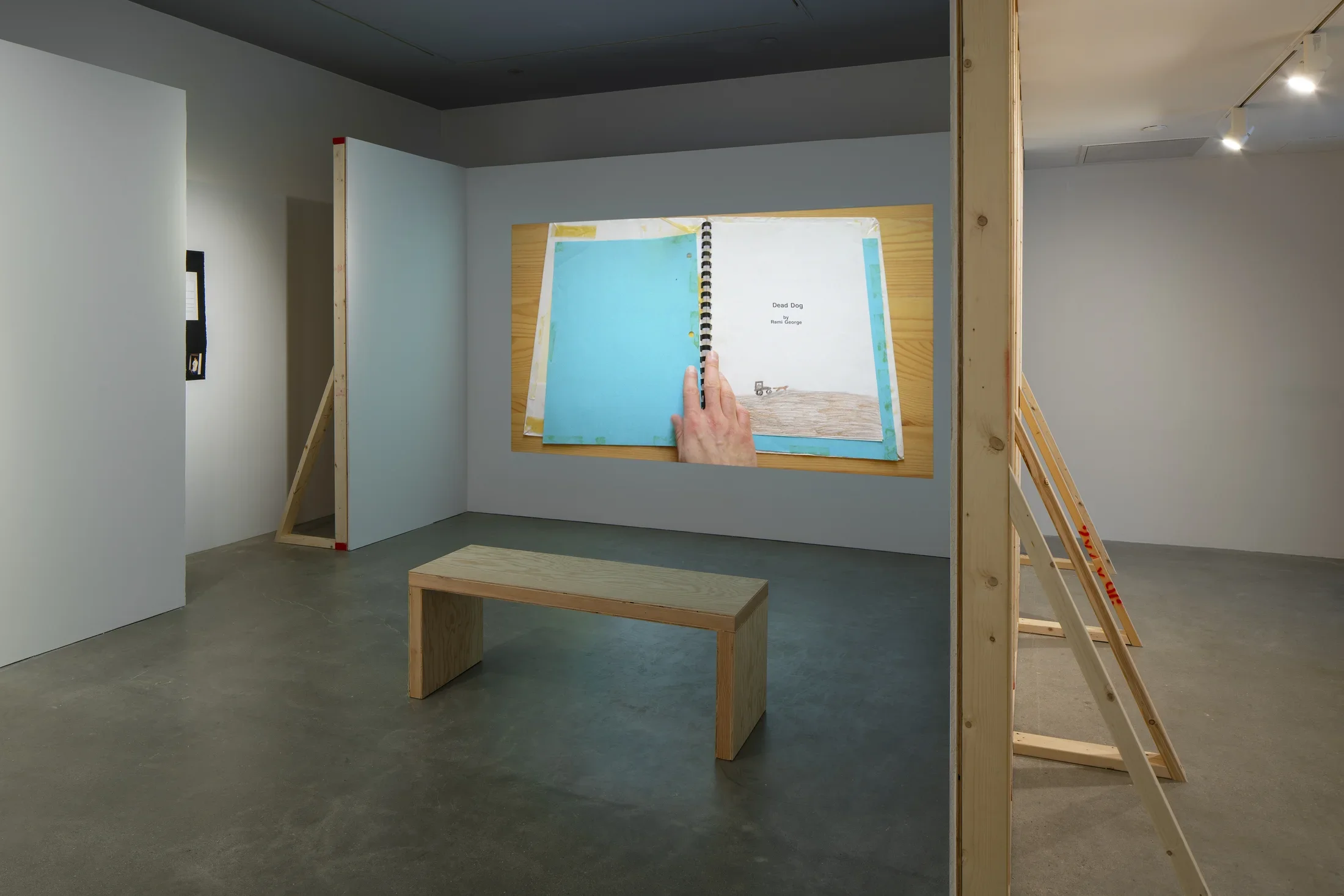 In a constructed alcove, a projected still of a child’s drawing titled “Dead Dog” in an old notebook with bright blue cover