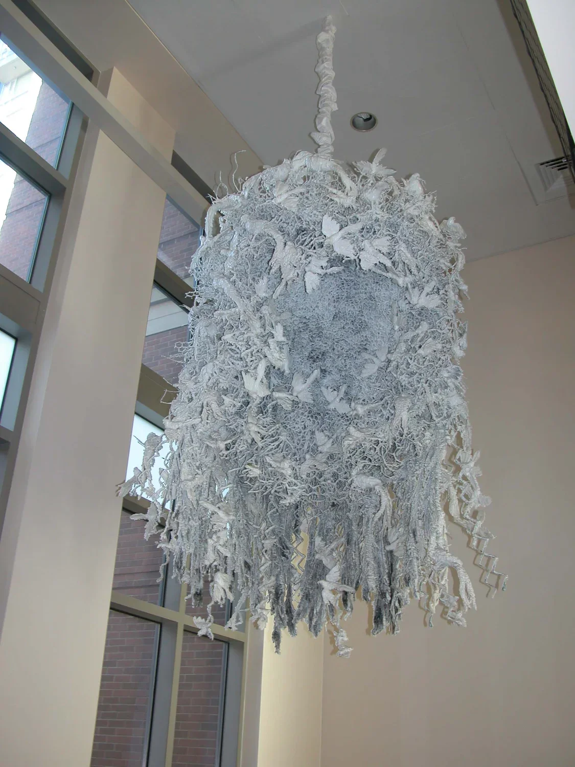 Sculpture hanging from a ceiling made of wax, wire mesh, found objects, and mixed media