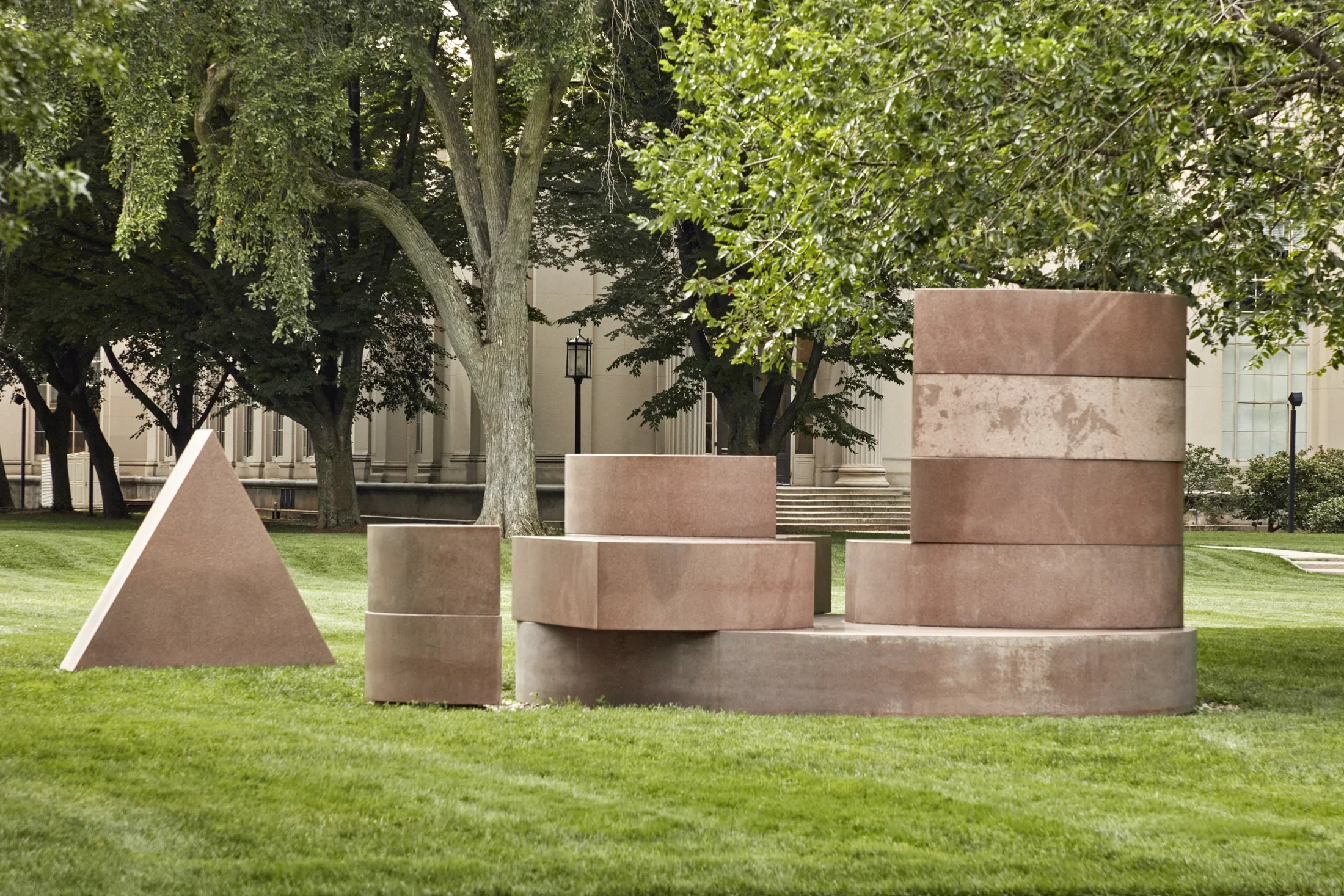 Pink Laurentian granite sculpture featuring geometric shapes on a lawn.