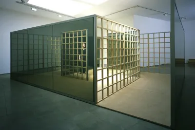 Installation view of a sculpture that resembles a building with lots of mirrors and a grid running along the side.