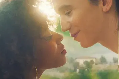 Two females face each other as if they are about to kiss, sunlight peaks between their faces.