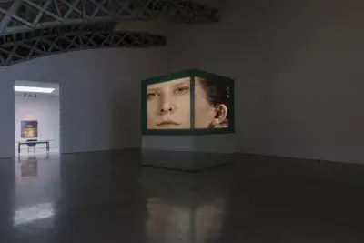 Installation view of a 5 channel video on a large projector showing a woman's face.