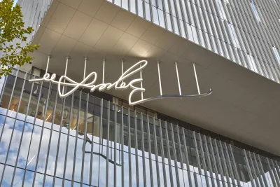 White LED sculpture of a signature being lit up hanging from a glass building.