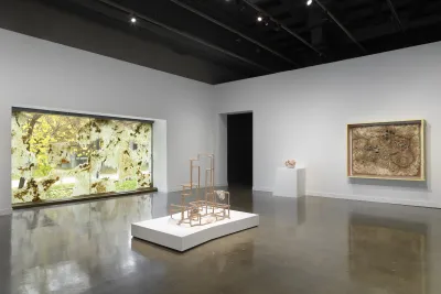 A window installation on the left featuring beeswax spread along the window, a geometric sculptural work in the center on a white platform, and along the back right wall, a smaller spherical sculpture sits on a white pedestal and a large rectangular sculpture hung on the wall.