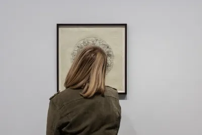 A woman with shoulder length blonde hair looks at a framed print on the wall.