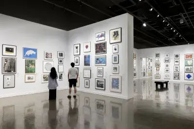 Two visitors look at artwork in frames during the Student Lending Art Program at the MIT List Visual Arts Center.