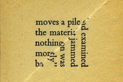 Image of a tan square piece of paper with black text. The paper in the front is folded in half diagonally to the bottom right. The text on the partly covered paper reads &quot;moves a pile the materi nothing more b&quot; and text on the folded paper reads &quot;ad examined jammed on was ly&quot;
