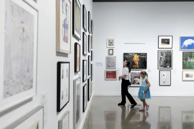 A woman and young girl look at artwork in frames during the Student Lending Art Program at the MIT List Visual Arts Center.