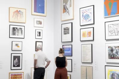 Two visitors look at artwork in frames during the Student Lending Art Program at the MIT List Visual Arts Center.