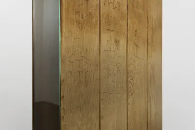Detail of hand-scratched names and initials on four planks of salvaged sauna cedar wood. A panel of glass is visible on the left side edge of the sculpture.