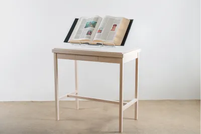 Image of a light cream wooden table displaying an open encyclopedia book within in a white walled room.