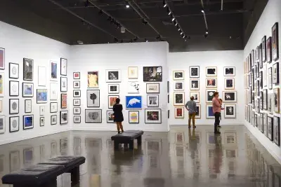 Installation view with framed artworks and a group of people gathered in the center.