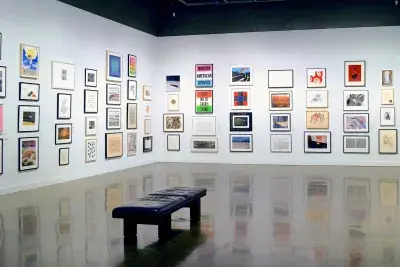 Installation view with framed artworks lining the walls floor to ceiling and a leather bench in the center of the gallery.