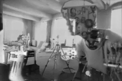 A woman’ s face and torso, turned 45 degrees towards the camera, is shown inside (or in front of) a studio space filled with electronic equipment. The woman is half substance and half outline: her shirt is solid, but most her face is a window into another image that shows neatly looped cables hanging on a wall. There is something amiss about the studio space too: while objects such as a tripod can be clearly discerned, other portions feature inverted tones and other forms of electronic manipulation.