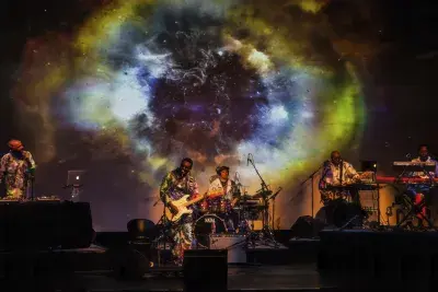 Image of a live musical performance, with five band members on stage in front of a projection of a galaxy.