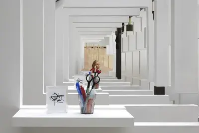 Image of a series of white walls with a window that has a view of the next white wall with a window. There is a cup with office supplies on the window ledge.