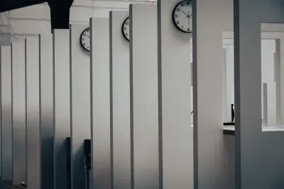 Image of a series of white walls with a window that has a view of the next white wall with a window. There is a analog clock hanging on every wall.