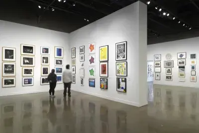 Installation view with framed artworks hanging on the walls salon style and two people standing beside each other in the center.