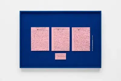Three pink notecards with handwriting in black pen on top of a dark blue background inside of a black frame that hangs on a white wall.