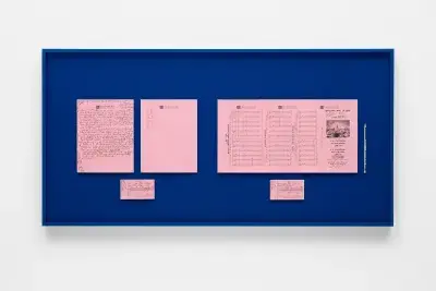 Three pink notecards with handwriting in black pen on top of a dark blue background inside of a black frame that hangs on a white wall.