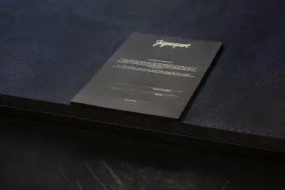 Image of a contract on black paper with gold text on top of the edge of a dark navy printed table.