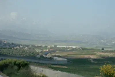 A border wall amongst a green landscape with hazy fog in the distance..