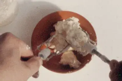 Aerial view of two hands mixing a white cream with hand mixer whisks in each hand.