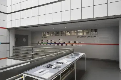 A large vitrine encasing black and white photos in the middle of an open atrium. A colorful timeline with images is adhered on the wall behind.