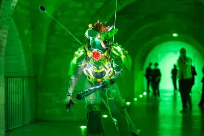 Image of a figure on rollerblades skating down a arched tunnel wearing a light-up vest and two reflective driveway markers as antenna. The entire spaced is washed in bright green light.