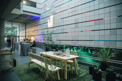 An event is held in the lobby of the Weisner Building outside of the List Center galleries. The focal point is a table surrounded by plants and special lighting.