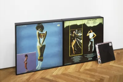 Multple framed images in Nayland Blake's series Controversey rest by a wall.