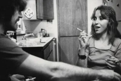 A black and white photo of a girll smoking a cigarette and a man in a flannel shirt.