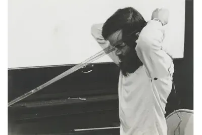 Tony Conrad holds a strip of film up to his face in a performance.
