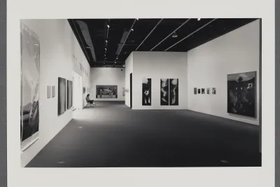 An installation view of the exhibition Nude, Naked, Stripped. A gallery attendant sits by the window around multi media artworks.