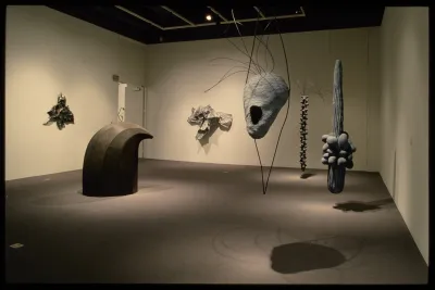 Organically shaped sculptures hang from the ceiling and walls. Each sculpture is spotlit, creating shadows on the floor.