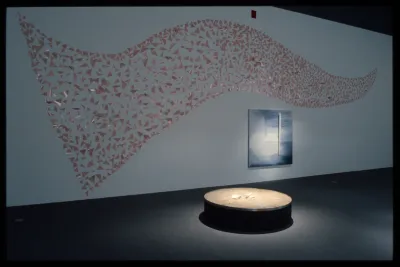 A performer places triangular pieces of paper on a spotlit red table top. Viewers sit in front in the darkness.