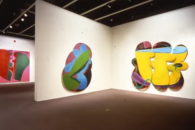 Three bright colored abstract paintings hung on walls, a rectangle shaped canvas and two irregular shapes with curved edges.