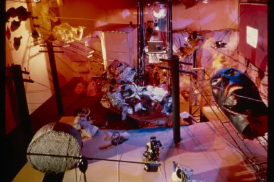 View from above of an environmental installation of an abstract mechanical landscape. A person sits in the middle of the installation.