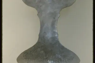 A metal sculpture in the shape of a cup or chalice of some kind. The light from the gallery reflects off of its surface. 