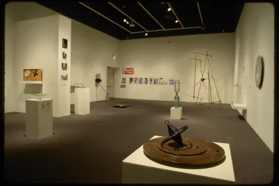 An installation view of hanging works and sculptures. Many sculptures take on the form of clocks, dials, or hourglasses.