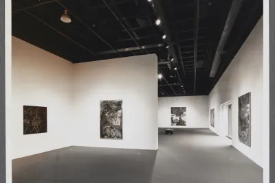 Large abstract paintings line the gallery walls as a bench sits in the center of the gallery. 